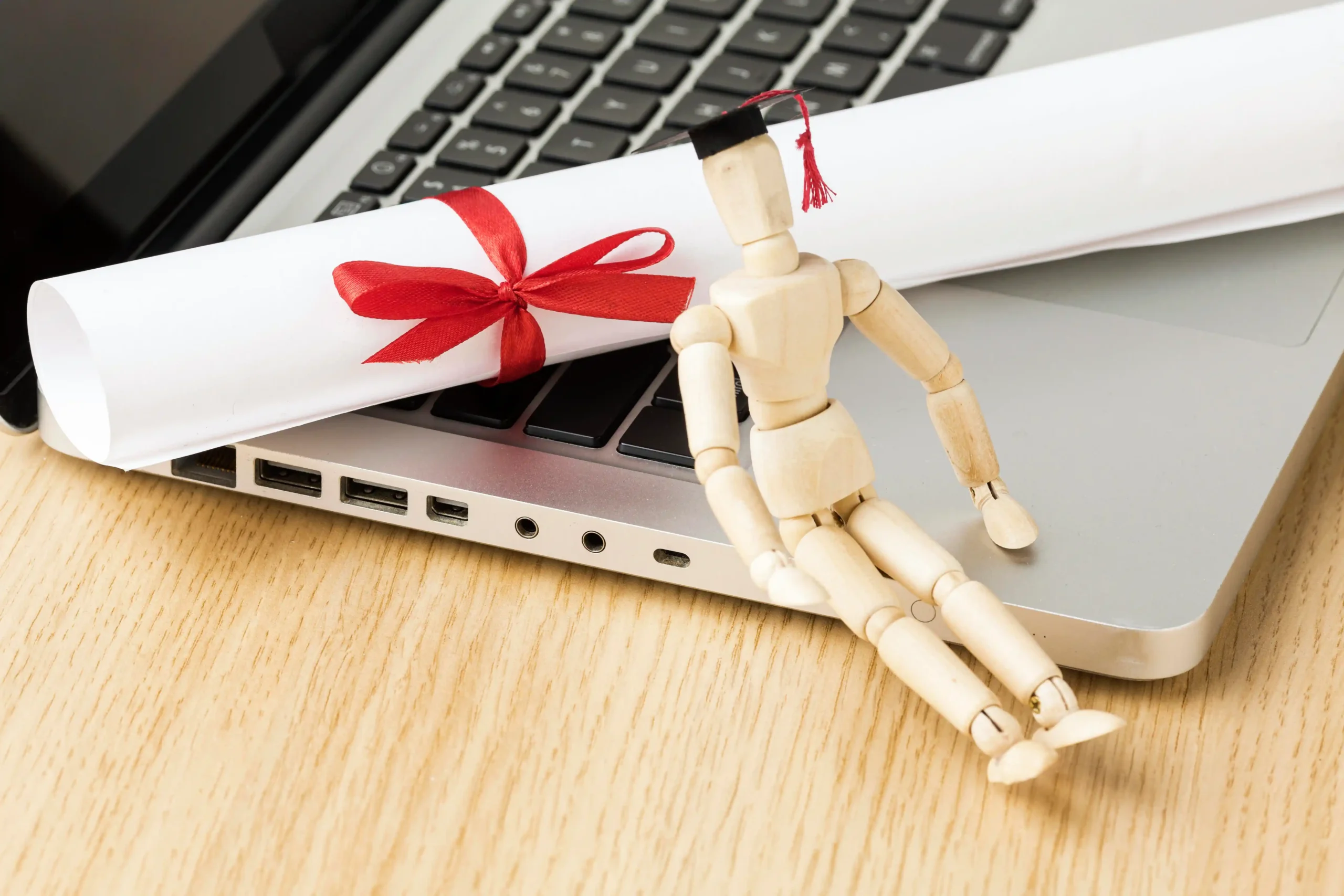 high-angle-laptop-with-wooden-figurine-academic-cap