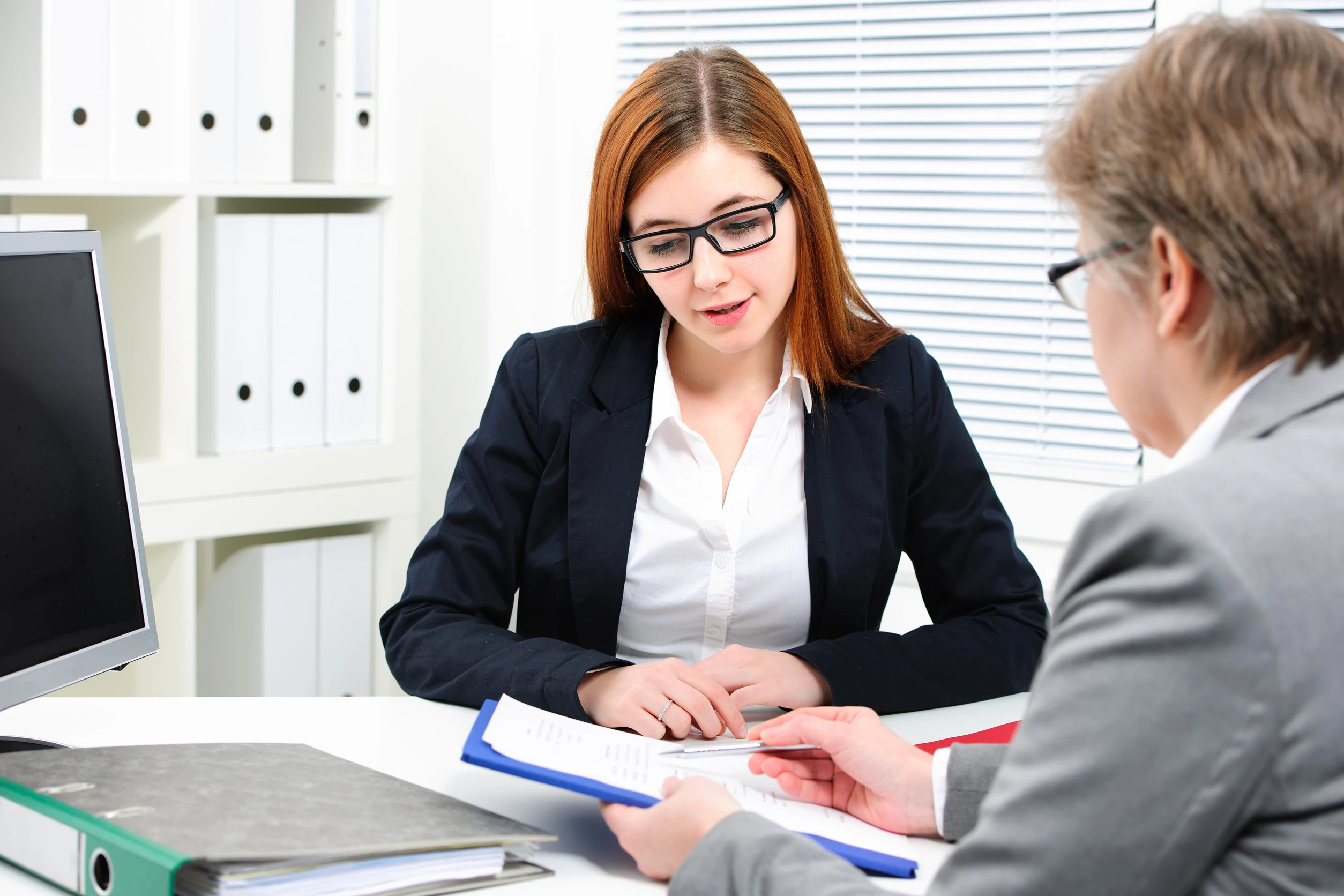 In a modern office setting, two professionals engage in a discussion, reviewing important documents. 